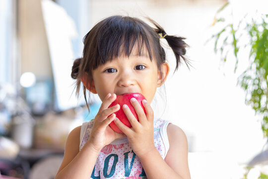 Portrait​ image​ of​ 2-3 yeas​ old​ of​ baby.​ Happy​ Asian child girl eating and biting an red apple. Enjoy eating moment. Healthy food and kid concept.​