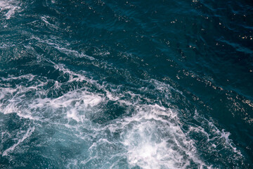 Fototapeta na wymiar Turquoise blue sea with foam and ripple. Cruise ship trail on blue ocean surface. White foam on sea texture