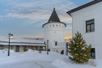 Fototapeta na wymiar Winter in the Tobolsk Kremlin (Russia). One of the round white towers in the evening against the backdrop of a sunset yellow-orange blue sky. young pine tree, lanterns and old buildings of the Kremlin