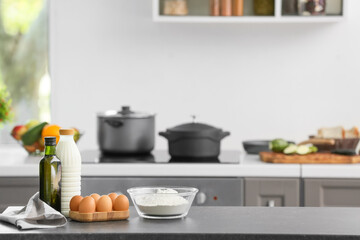 Fototapeta na wymiar Bowl with flour, eggs and bottle of milk on table in modern kitchen