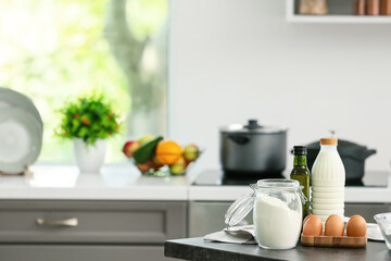 Jar with flour, eggs and bottle of milk on table in modern kitchen