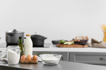Bowl with flour, eggs and bottle of milk on table in modern kitchen