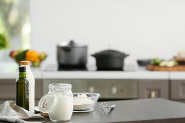 Bowl with flour, whisk and bottle of oil on table in modern kitchen