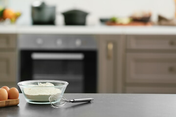 Bowl with flour, eggs and whisk on table in modern kitchen