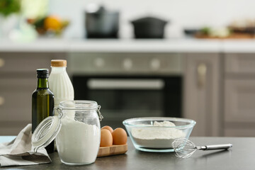 Bowl with flour, eggs and bottle of milk on table in modern kitchen