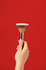 Hand with makeup sponge and brush on color background