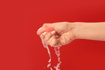 Hand squeezing wet makeup sponge on color background