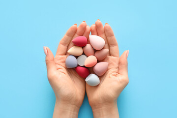 Hands with makeup sponges on color background