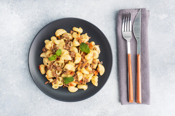 Stewed pasta with minced beef and vegetables, macaroni in Navy style on a plate. grey concrete background. Copy space.