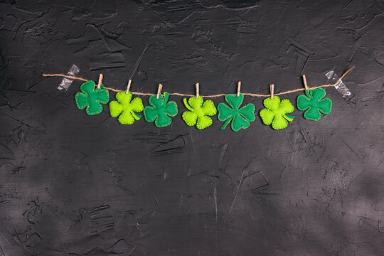 Garland of decorative clover leaves on clothespins on a black background with copy space.