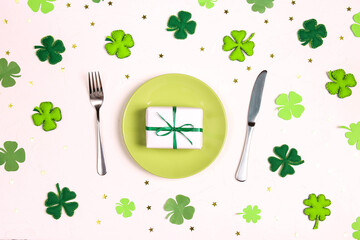 Festive table setting for St.Patrick's day with cutlery, decorative clover leaves, gift and gold stars on white table.