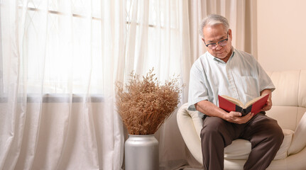 Asian Senior man reading book and stay alone at home. Retirement age lifestyle.
