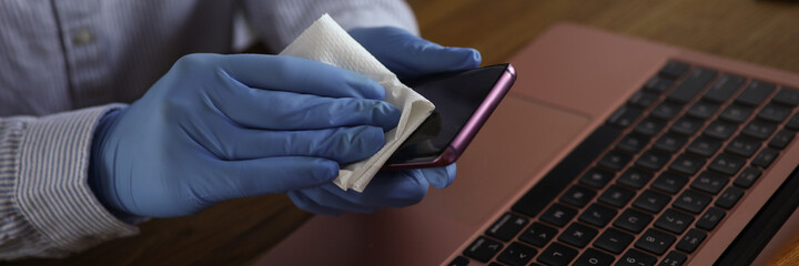 Woman hand in protective gloves hold smartphone with napkin closeup