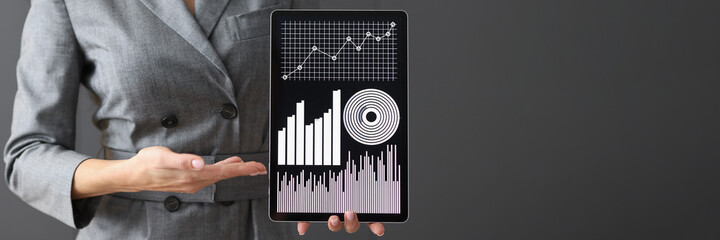 Businesswoman holding digital tablet with graphs and charts in her hands at office closeup