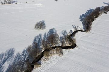 a curvy stream meanders through the snowy winter landscape - aerial view 
