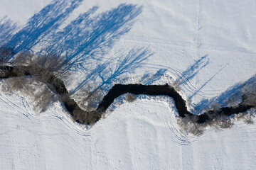 a curvy stream meanders through the snowy winter landscape - aerial view 