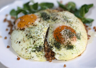 Fried egg with buckwheat and arugula on white plate