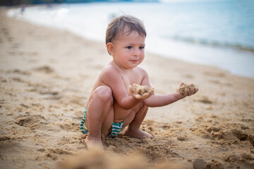 Fototapeta na wymiar cute toddler kid playing in the sand by the sea