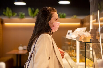 beautiful adult woman in medical mask orders food and drink in cafe
