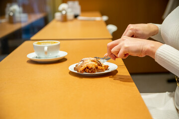 woman cuts croissant and drinks coffee at a table in a cafe