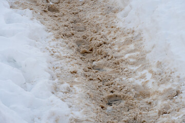 A narrow path in a snowdrift after a snowstorm. footprints in the snow. The icy road is covered with sand and reagents.