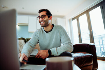 Smiling mixed race business man typing on laptop sitting on couch working from home