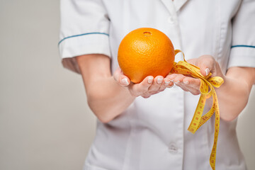 nutritionist doctor healthy lifestyle concept - holding orange fruit and measure tape