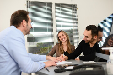 Young couple signing documents in a business bank insurance office with a professional real estate agent