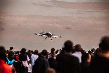 Fototapeta na wymiar Crowd of unrecognizable blurry people, aviation show enthusiasts watching the evolutions of an airplane, selective focus on the plane.