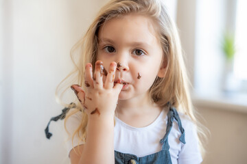 little blonde cute girl got her chocolate fingers dirty and licks them.