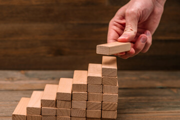 Business concept - hand builds a ladder from wooden blocks. Driving business at the peak concept.