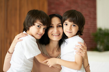 Portrait of two latin children, little twin boys smiling at camera and hugging their mom, spending time together at home