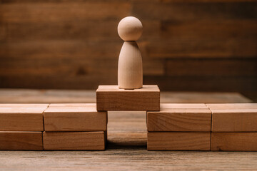 Wooden figurines of people stand on the planks of the bridge opening made of wooden blocks as a concept of risks in business and strategy