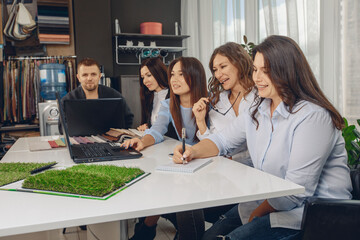 Team of five people sitting at a table working together colleagues looking at a laptop and writing in a notebook in the office. Productivity concept