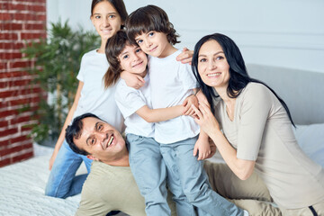 Family time. Portrait of happy latin family, parents and children smiling at camera while spending time together at home