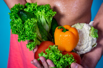 Slim male body and fresh vegetables. Healthy food and sports. Diet and weight loss. Blue background.