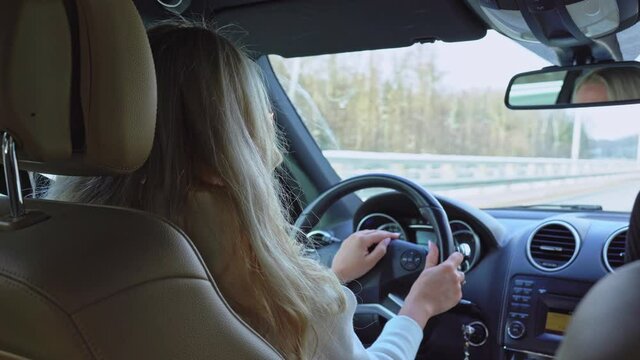 Back view of blonde long haired woman driving a car on a highway at winter sunny day