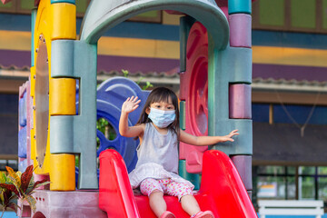 Portrait image of 2-3 yeas old baby. Happy Asian child girl smiling and wearing fabric mask,​ She playing with slider bar toy at the playground, social​ Distance,​ Learning and active of kids concept.