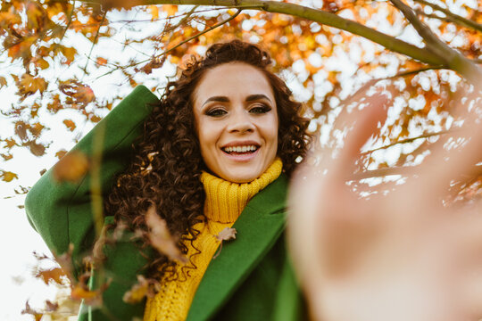 The girl gleefully smiling in the autumn park stretched forward her hand closing from the camera. High quality photo