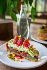 Pistachio strawberry tart filled with strawberry jam on wooden background.