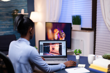 Dark skinned woman playing games on laptop in home office at night. Professional player checking digital video games on her computer with modern technology network wireless.