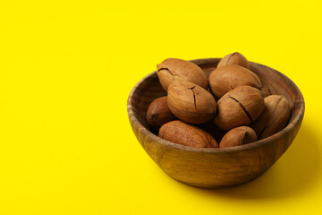 Obraz premium Bowl with tasty pecan nuts on yellow background