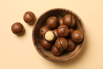 Bowl with tasty macadamia nuts on beige background
