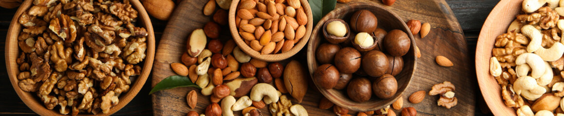 Wooden bowls with different nuts on wood background, top view