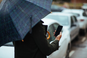 Male texting under umbrella on the city streets