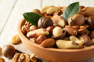 Bowl with different tasty nuts on white wooden background