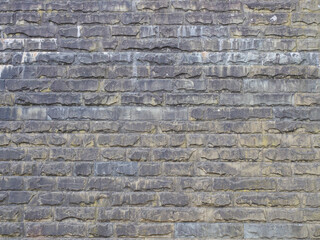 The wall with rough textured masonry is covered with stains and darkened. Not a geometric seamless pattern