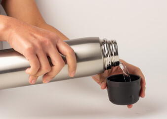 The hand was holding the stainless water bottle to pour water into the lid.