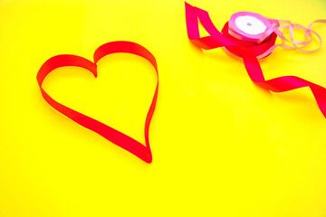 On a yellow background is a pink satin ribbon in the shape of a heart.Gift wrap.