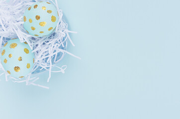 Fashion easter background - blue eggs with golden design in white nest closeup on blue color, top view.